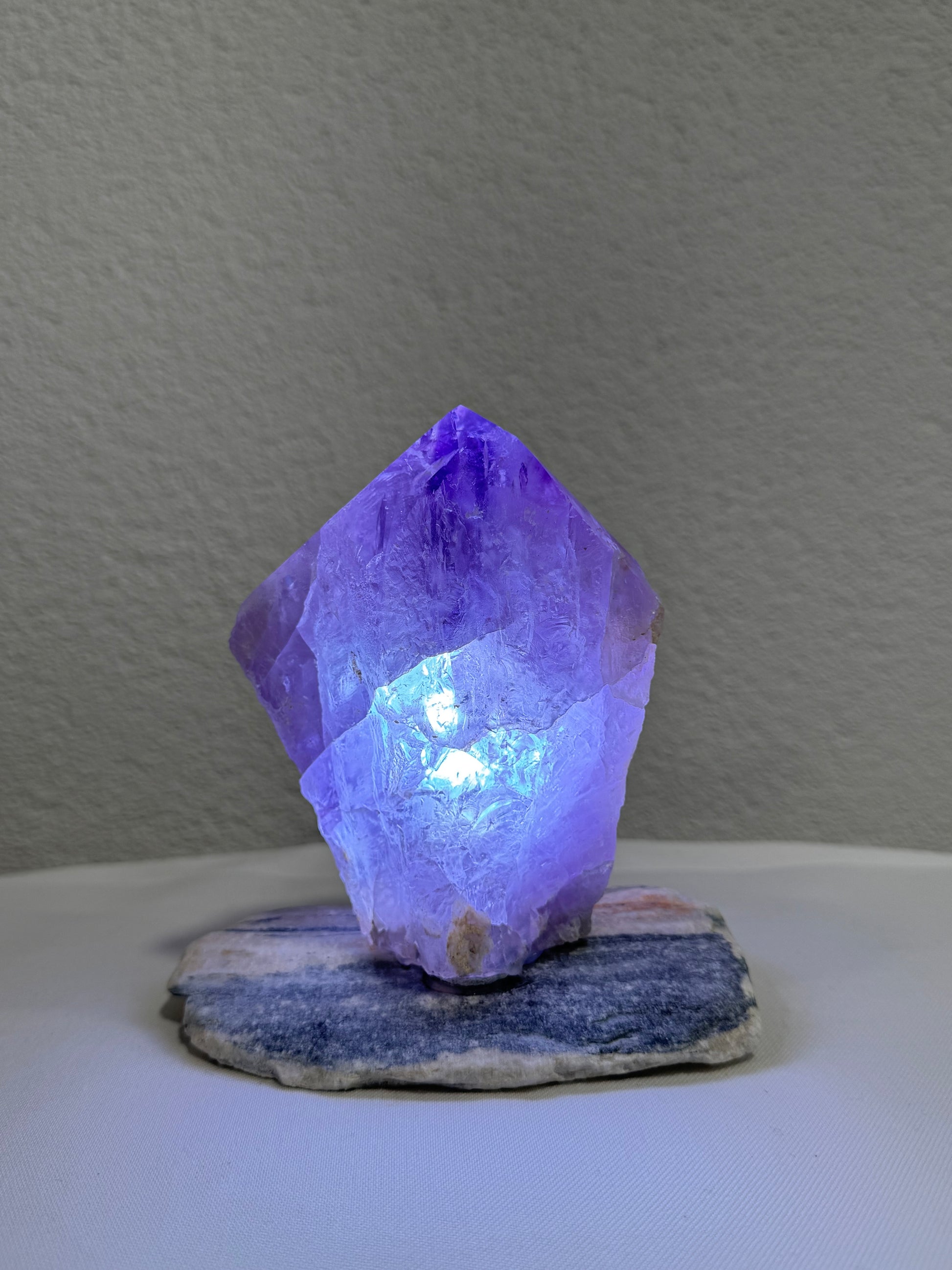 Ein violett leuchtender Amethyst-Kristall auf einem polierten Steinsockel, ideal für die Dekoration oder als spirituelles Element