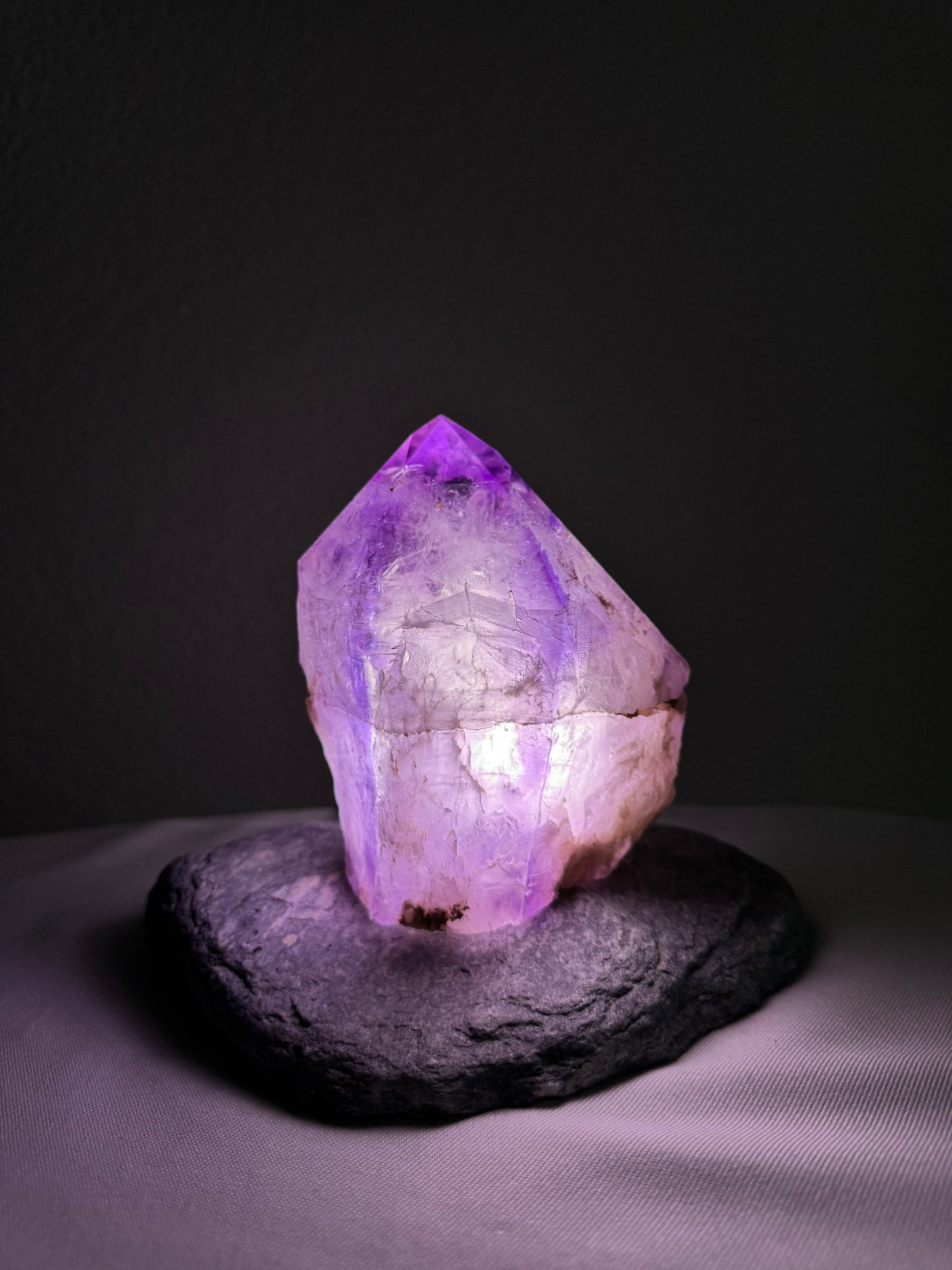 Beleuchteter Amethyst auf Natursteinsockel, einzigartige Dekoration für Wohnräume, funkelnder lila Kristall